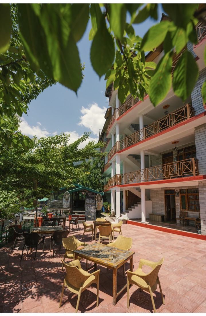 Courtyard seating below the building's balconies, framed by tree leaves