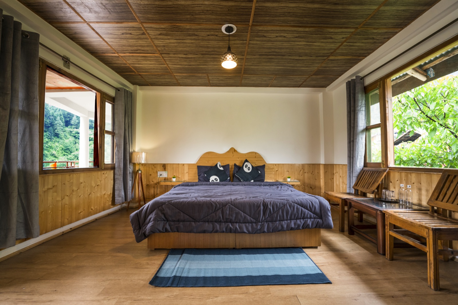 Private room, bed made, daylight and hillside view through the windows